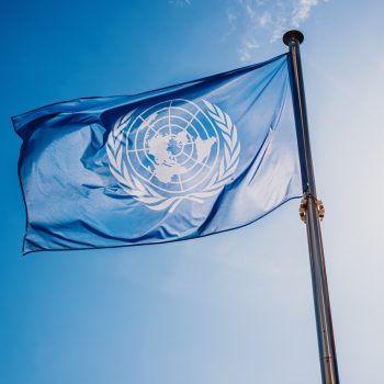 UN flag waved against the sun and blue sky.
